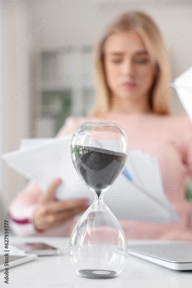 Hourglass on table of businesswoman in office, closeup. Deadline concept