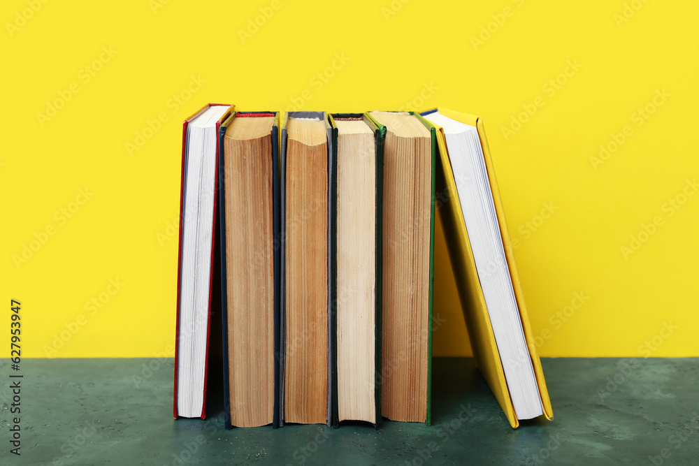 Books on green table against yellow background