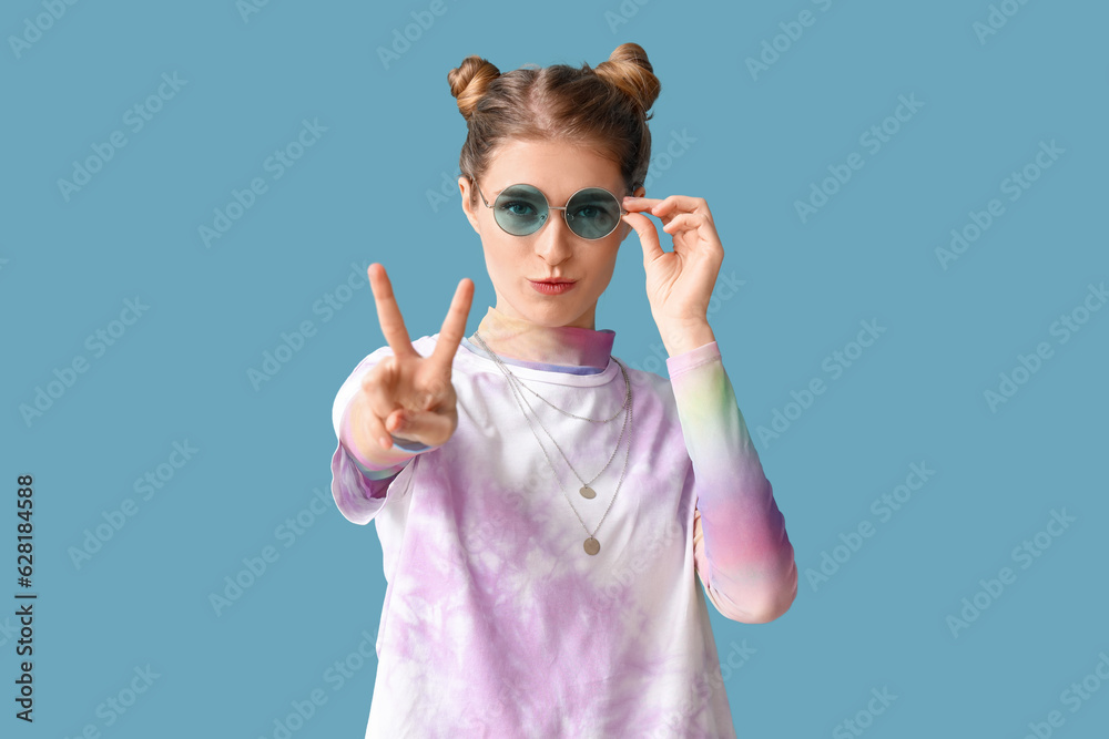 Young woman in tie-dye t-shirt showing victory gesture on blue background