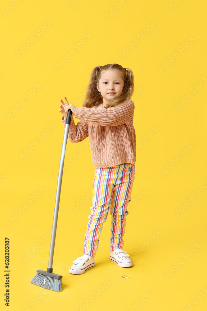 Cute little girl with broom on yellow background