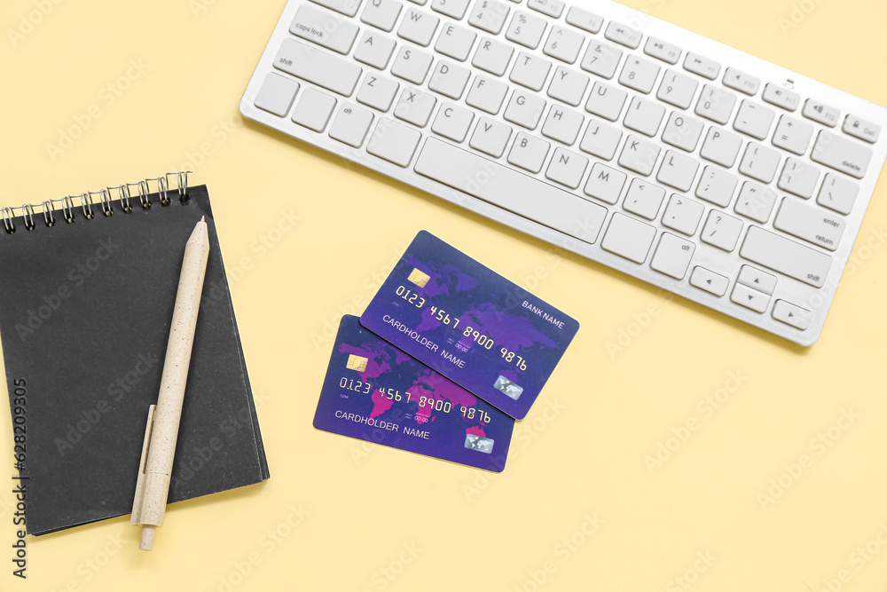 Keyboard with credit cards and notebook on pale yellow background