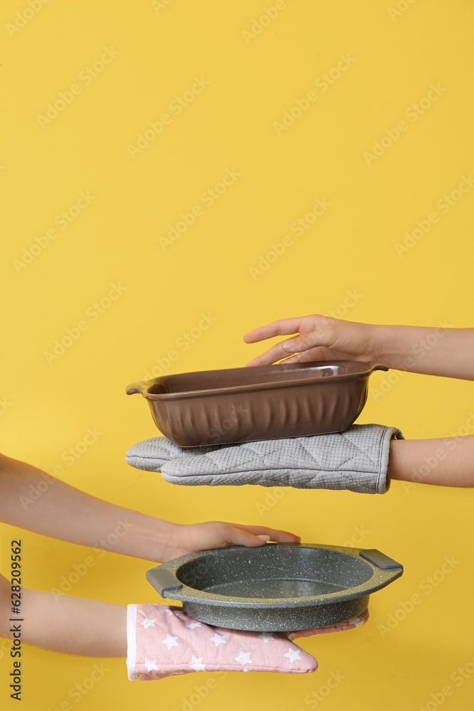 Female hands with baking forms and mittens on yellow background