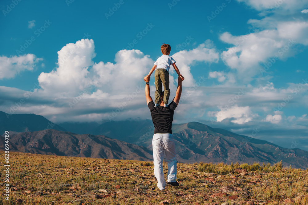 Boy standing on his fathers shoulders on mountains background