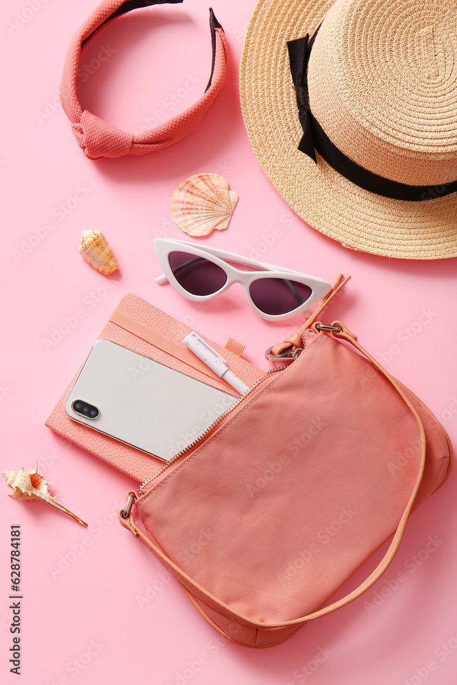 Stylish bag with mobile phone and different accessories on pink background