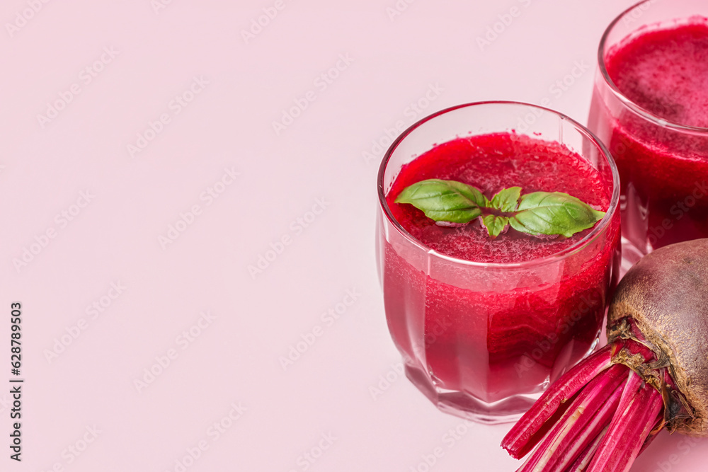 Glasses of healthy beet juice with basil on pink background