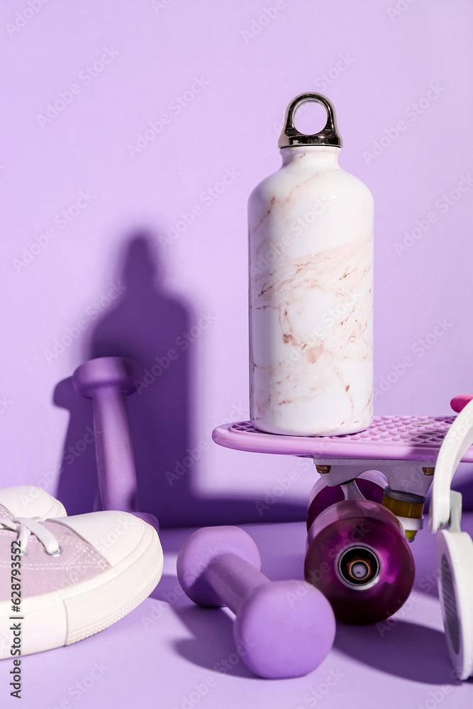 Bottle of water, skateboard, dumbbells and shoes on lilac background