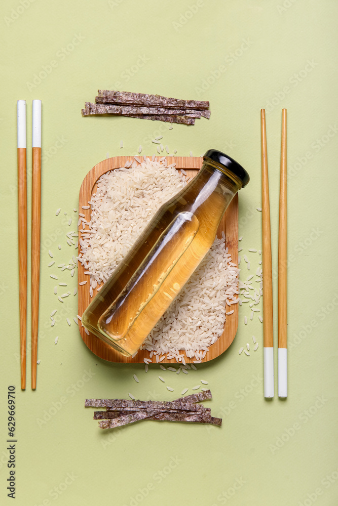 Composition with bottle of vinegar, rice, nori sheet and chopsticks on color background