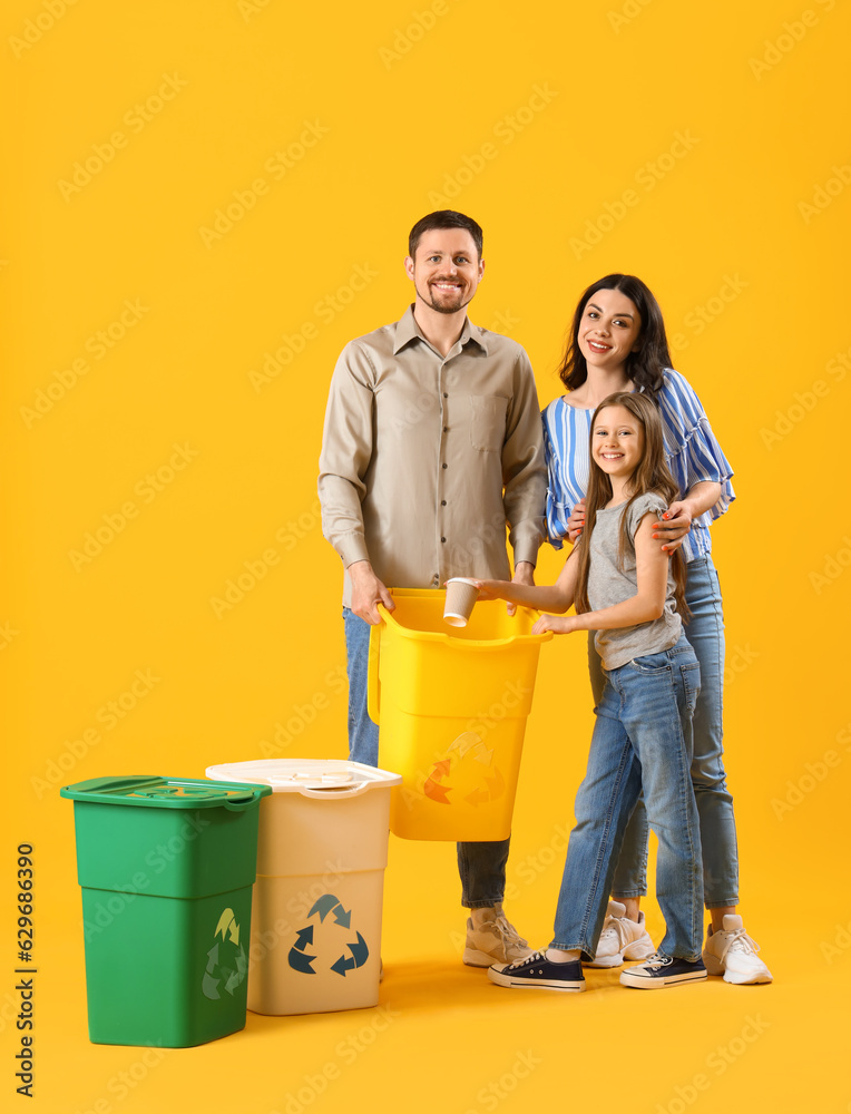 Little girl with her parents throwing paper cup in recycle bin on yellow background