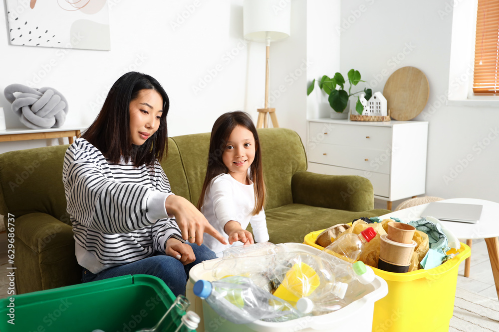 Asian mother with her little daughter sorting garbage in recycle bins at home