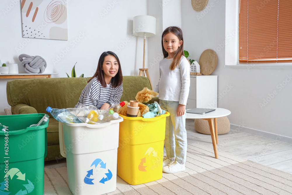 Asian mother with her little daughter sorting garbage in recycle bins at home