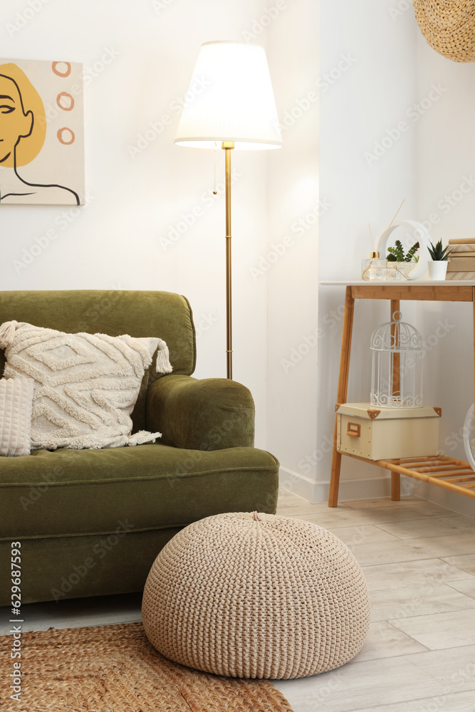 Interior of stylish living room with cozy green sofa, pouf and glowing lamp