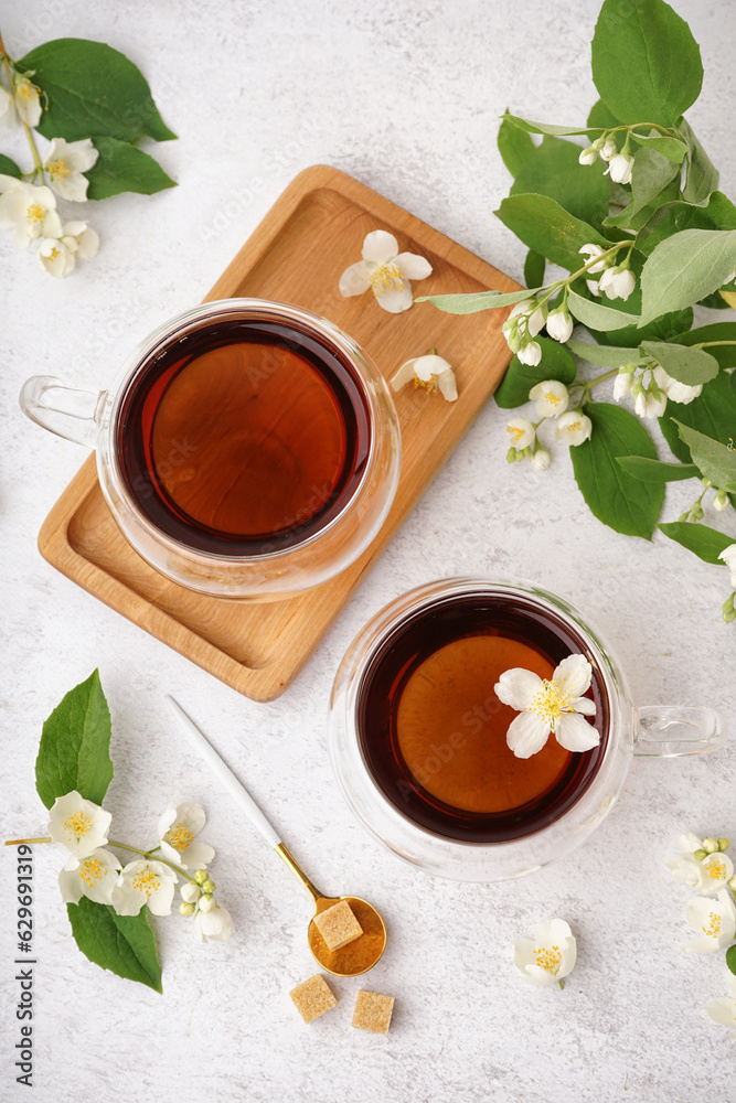 Glass cups of tea, sugar and beautiful jasmine flowers on light background