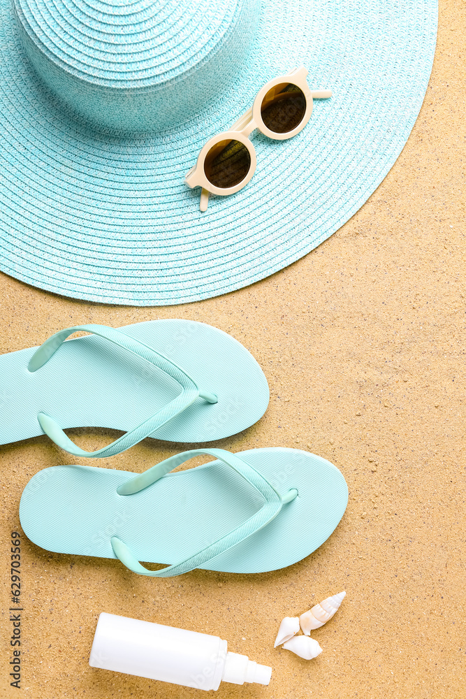 Straw hat, flip-flops, sunglasses and sunscreen cream on sand background