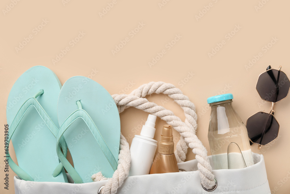 Female bag with beach accessories, sunscreen cream and bottle of drink on color background, closeup