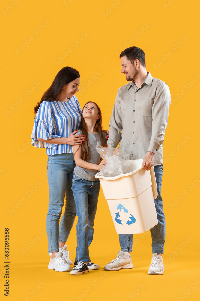 Little girl with her parents throwing plastic garbage in recycle bin on yellow background