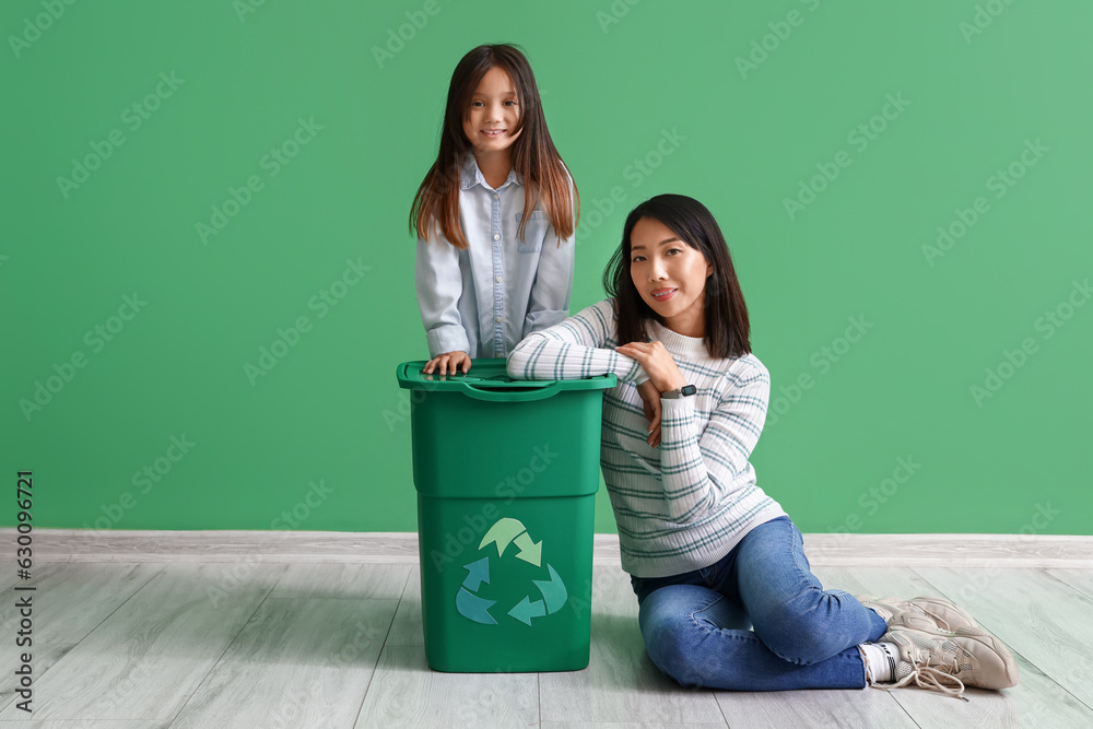 Asian mother with her little daughter and recycle bin near green wall