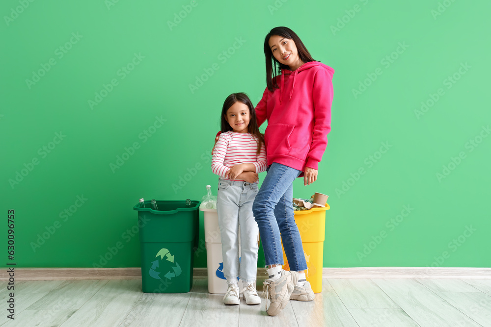 Asian mother with her little daughter and recycle bins near green wall