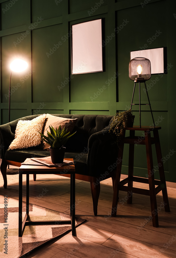 Interior of dark living room with green sofa, coffee table and glowing lamps