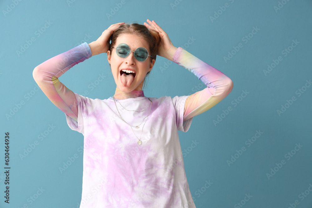 Young woman in tie-dye t-shirt showing tongue on blue background