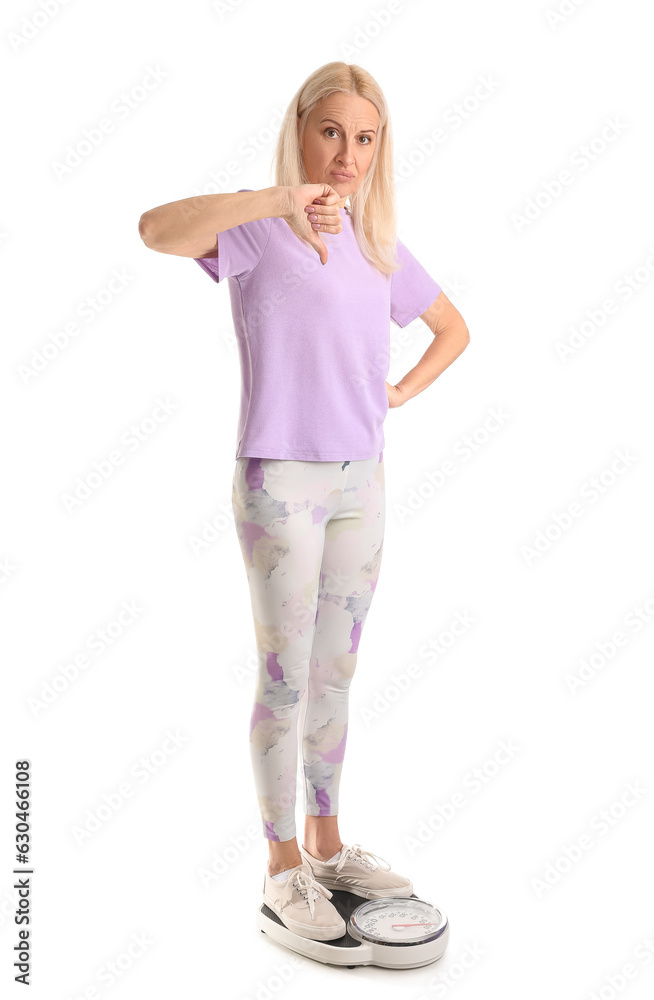 Upset mature woman showing thumb-down on scales against white background