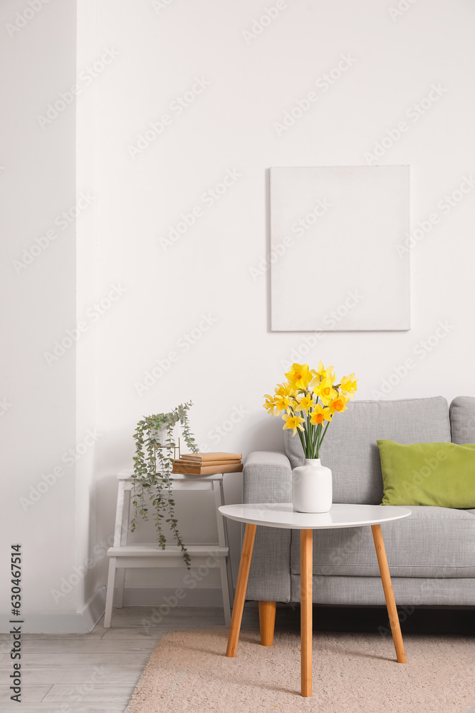 Interior of living room with grey sofa and blossoming narcissus flowers on coffee table