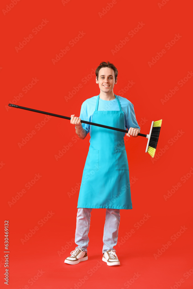 Male janitor with broom on red background
