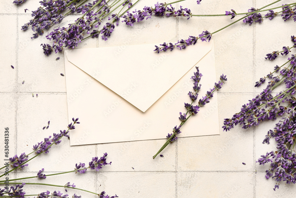 Branches of beautiful lavender flowers and envelope on light tile background, closeup