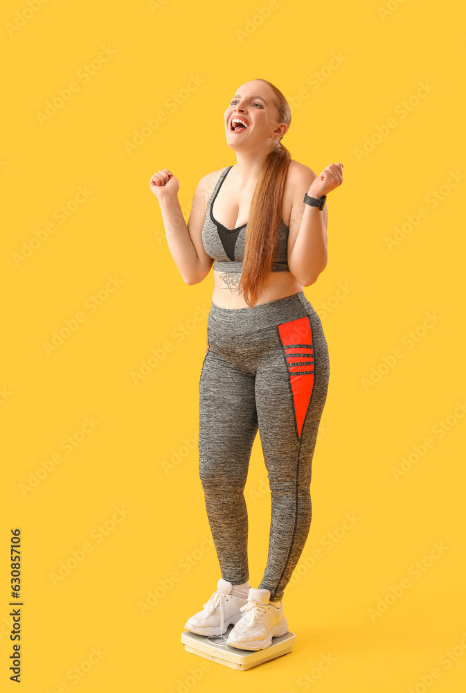 Young overweight woman measuring her weight on scales against yellow background