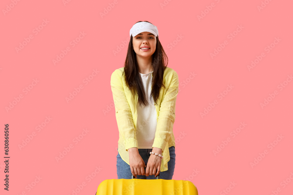 Young woman with suitcase on pink background