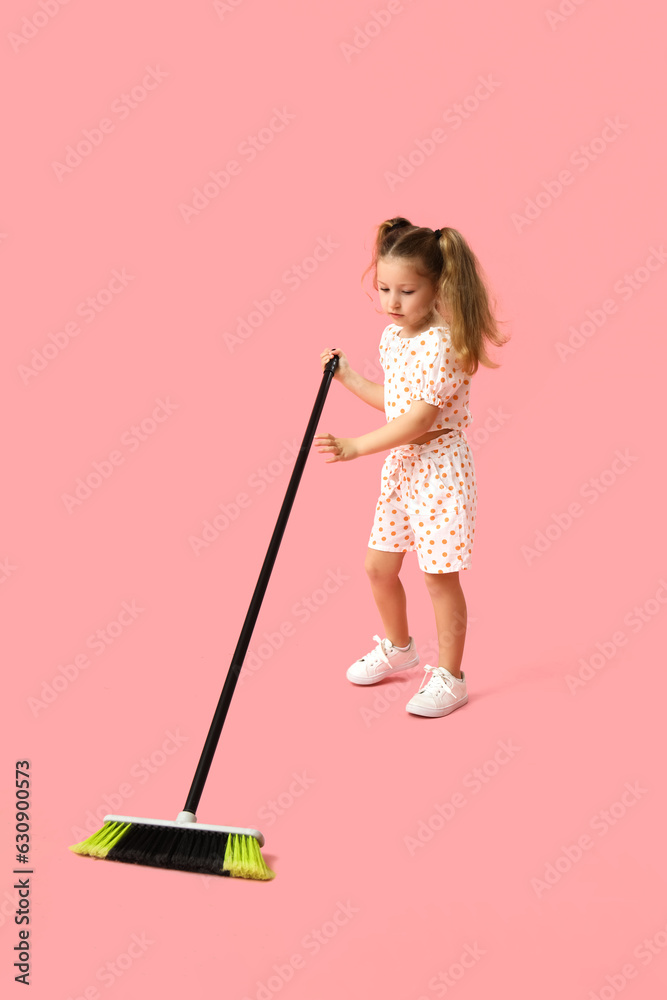 Cute little girl sweeping with broom on pink background