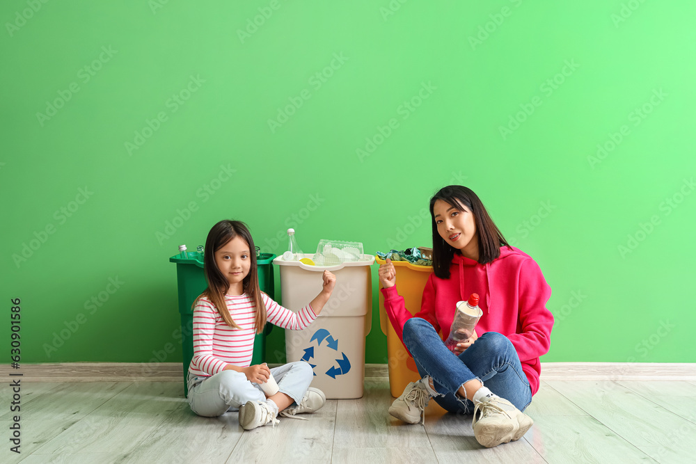 Asian mother with her little daughter pointing at recycle bins near green wall
