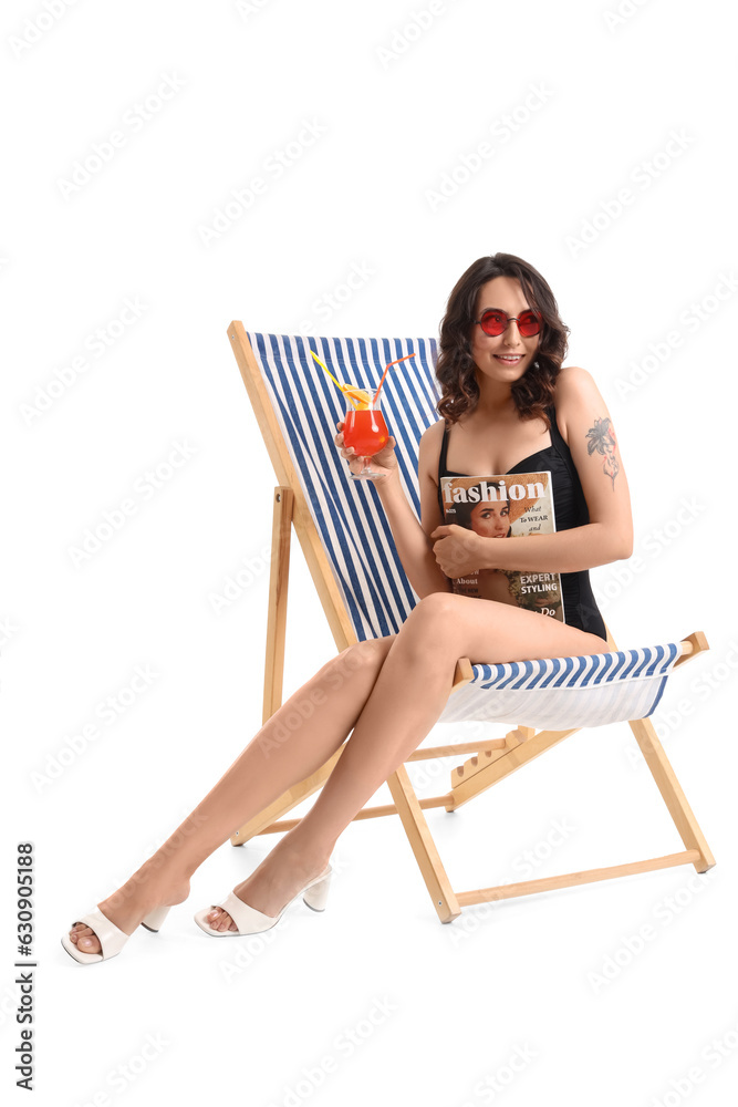 Young woman with cocktail and magazine in deck chair on white background