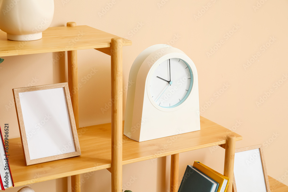 Clock with blank frame on shelf near beige wall
