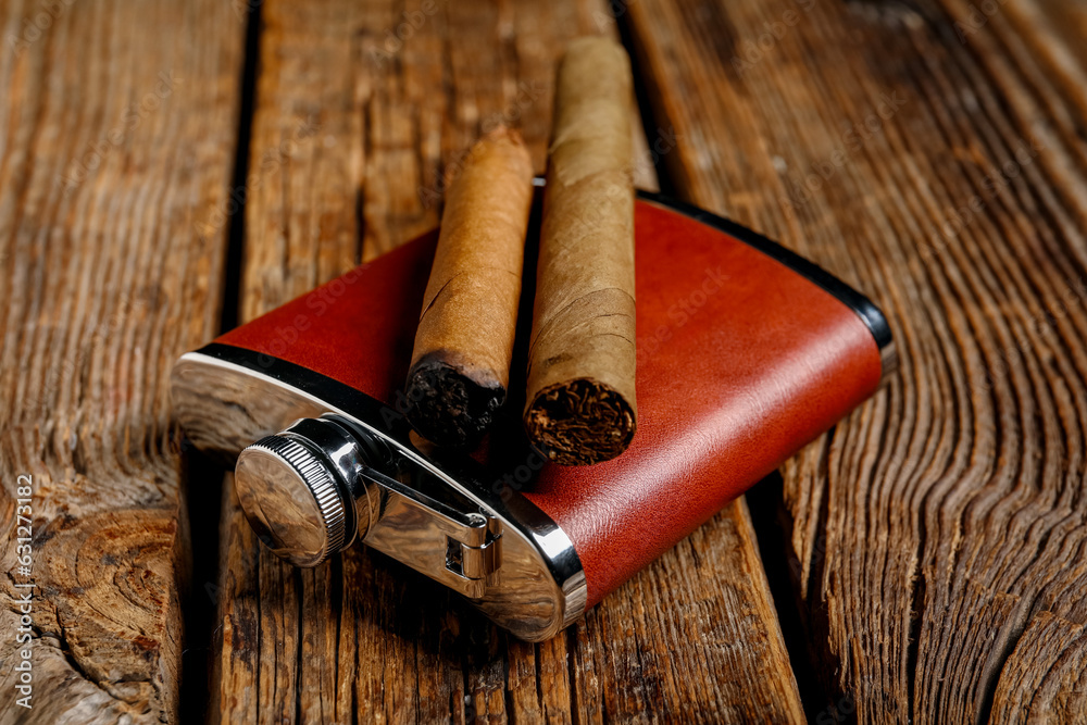 New hip flask with cigars on wooden background, closeup