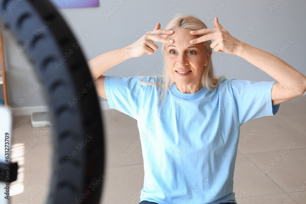 Mature physiotherapist doing face building exercise while recording video in rehabilitation center