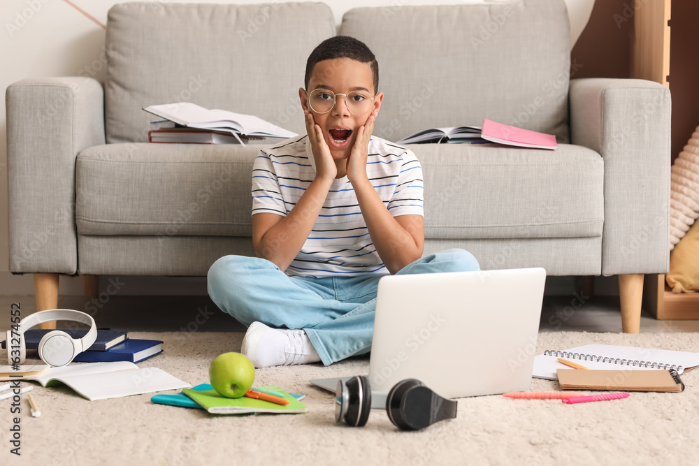 Surprised little African-American boy studying computer sciences online at home