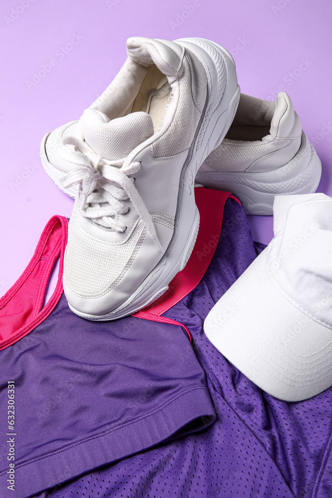Stylish female sportswear, shoes and cap on lilac background, closeup