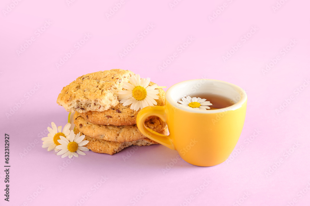 Cup of natural chamomile tea with cookies and flowers on pink table near yellow wall