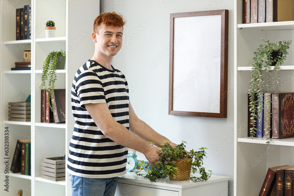 Young redhead man with houseplant at home