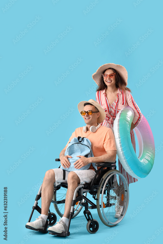 Young woman with her husband in wheelchair and inflatable ring on blue background