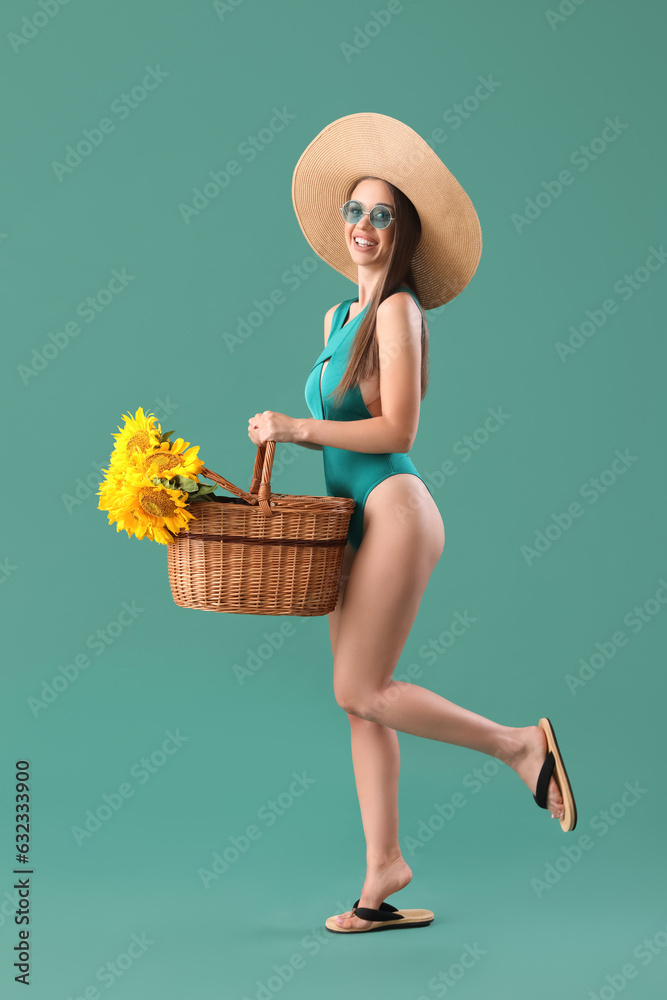 Young happy woman in swimsuit with wicker basket full of beautiful sunflowers on green background