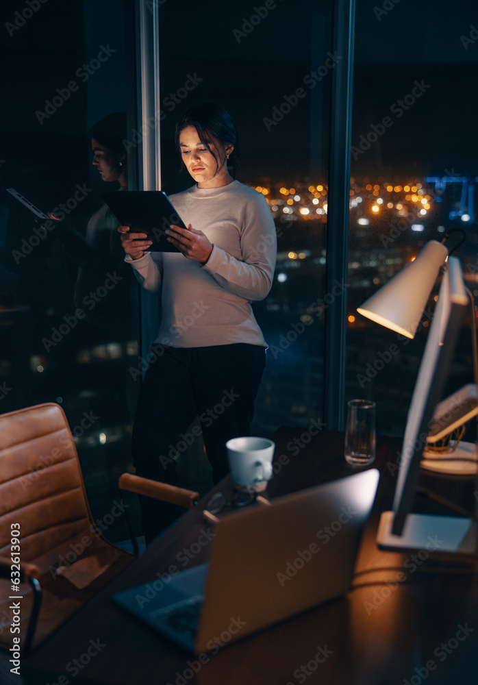 Business woman working late in her office, using a tablet to analyse data