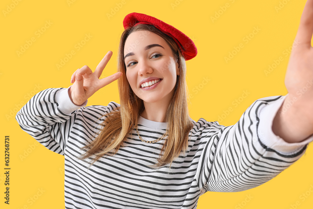 Young woman showing victory gesture on yellow background