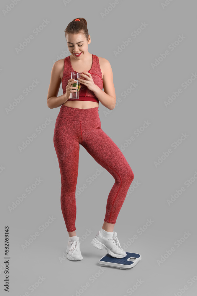 Sporty young woman with scales and glass of water on grey background