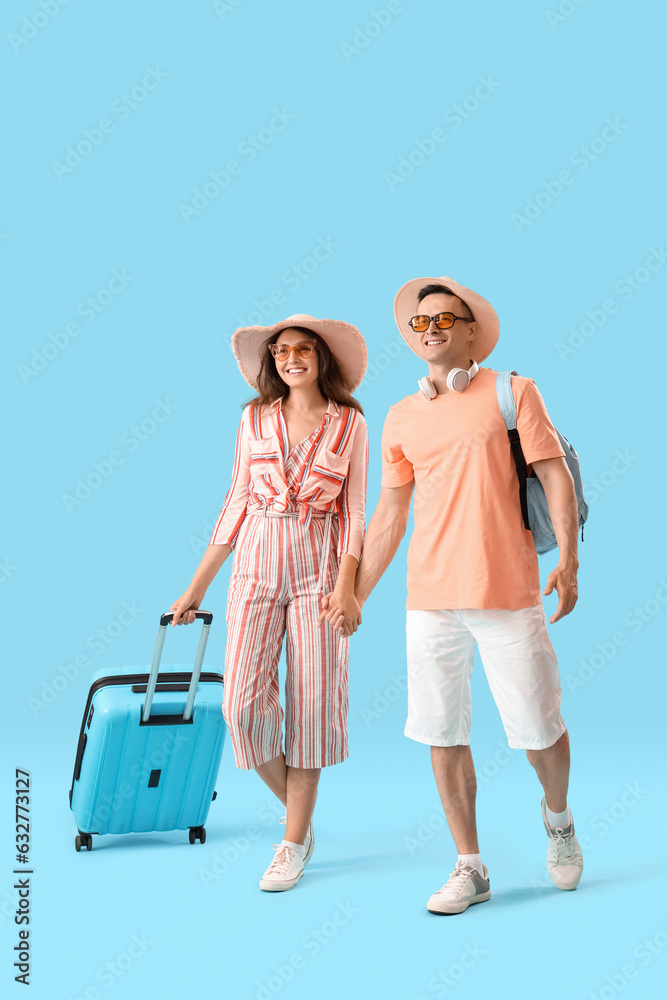 Young couple with suitcase holding hands on blue background