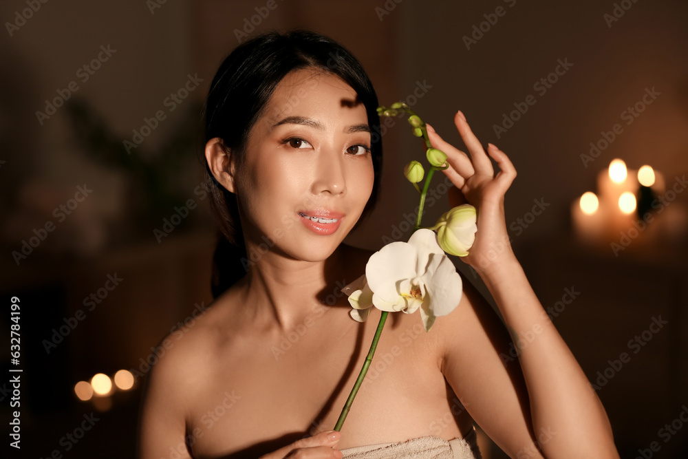 Pretty young Asian woman with orchid flowers in spa salon