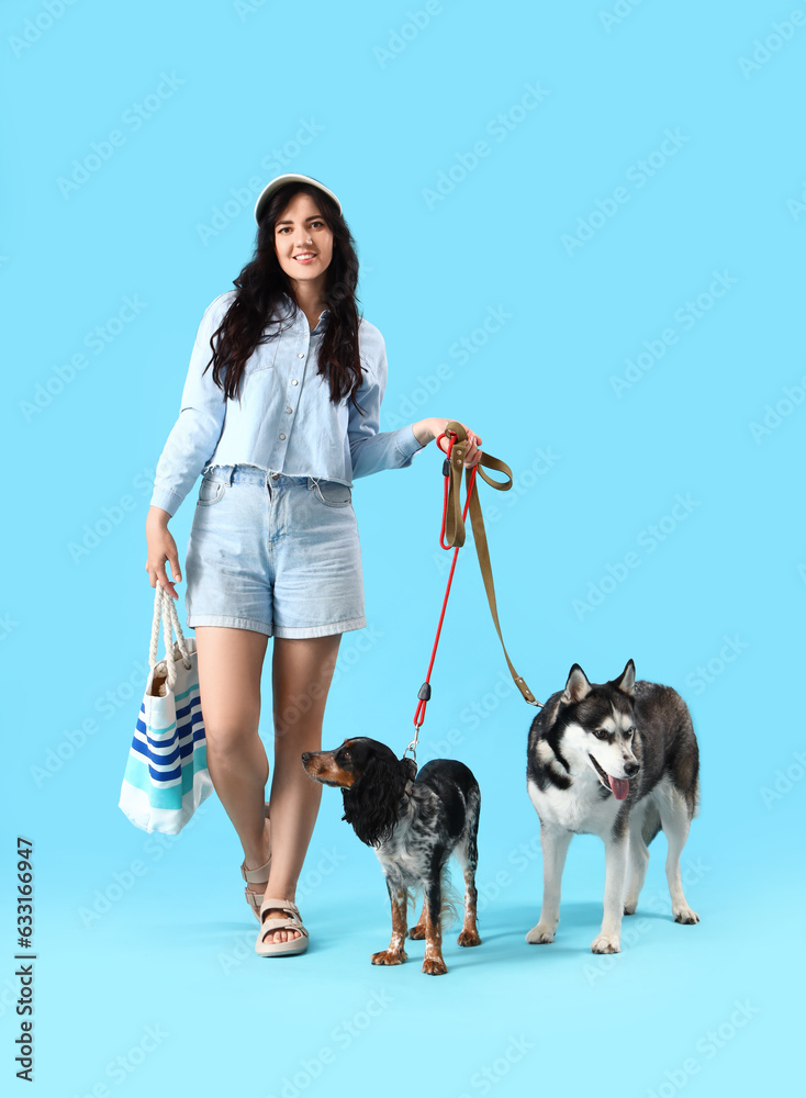 Young woman with cute dogs walking on blue background