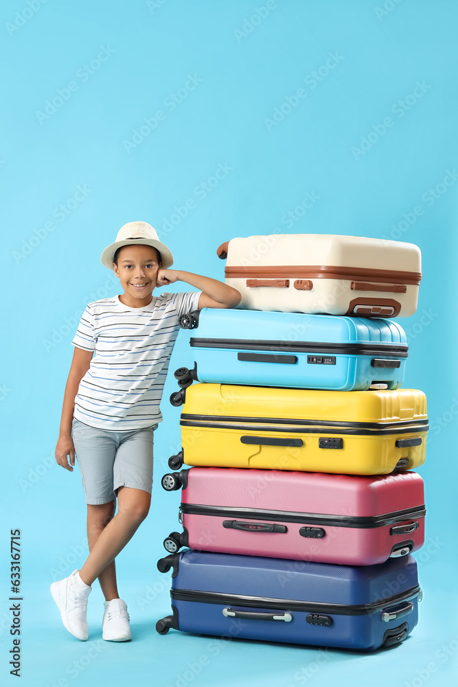 Little African-American boy standing near pile of suitcases on blue background