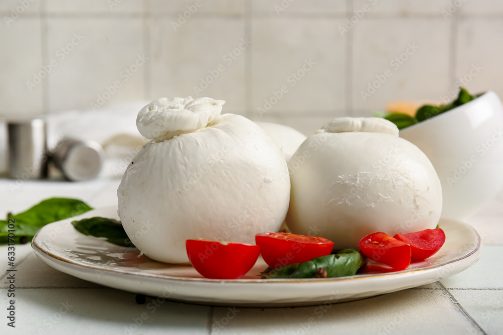 Plate of tasty Burrata cheese with basil and tomatoes on white tile background