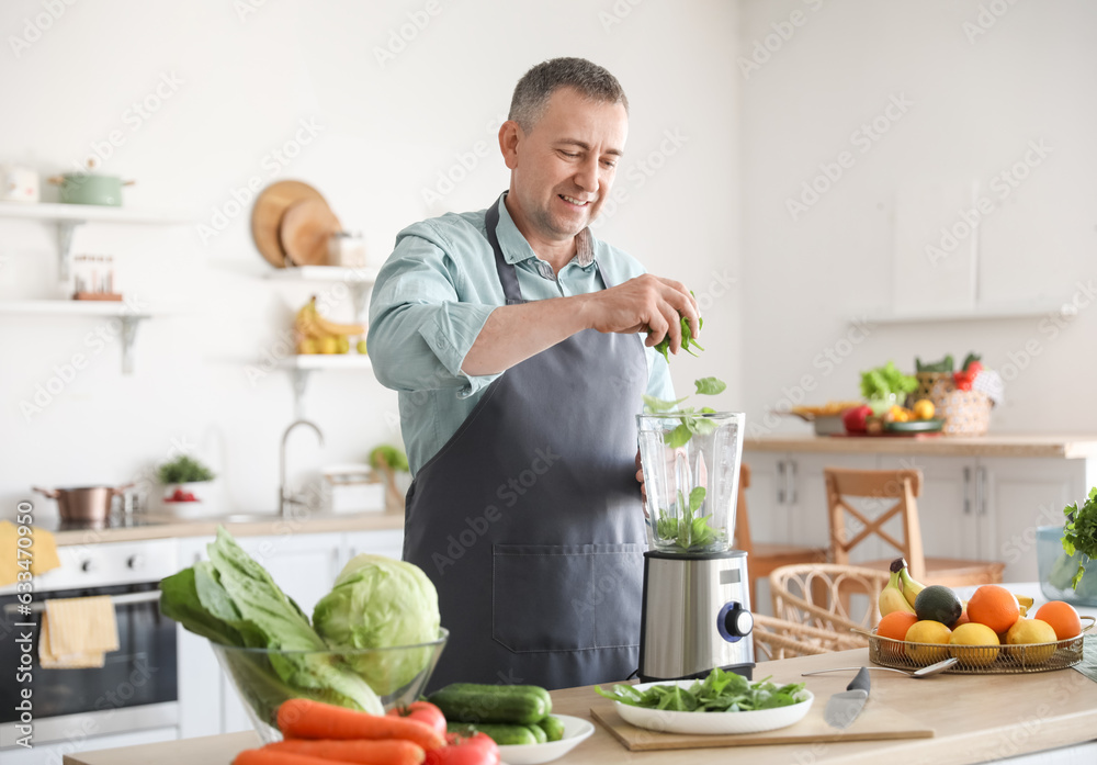 Mature man making smoothie with spinach in kitchen